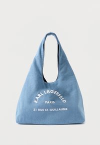 Bolsa de ombro azul em lona com um formato descontraído, apresentando texto branco: "KARL LAGERFELD PARIS 21 RUE ST-GUILLAUME." Textura suave, grande abertura.