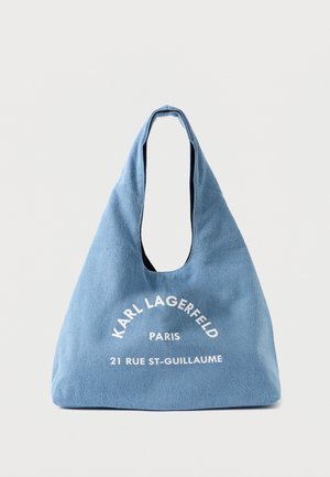 Bolsa de ombro azul em lona com um formato descontraído, apresentando texto branco: "KARL LAGERFELD PARIS 21 RUE ST-GUILLAUME." Textura suave, grande abertura.