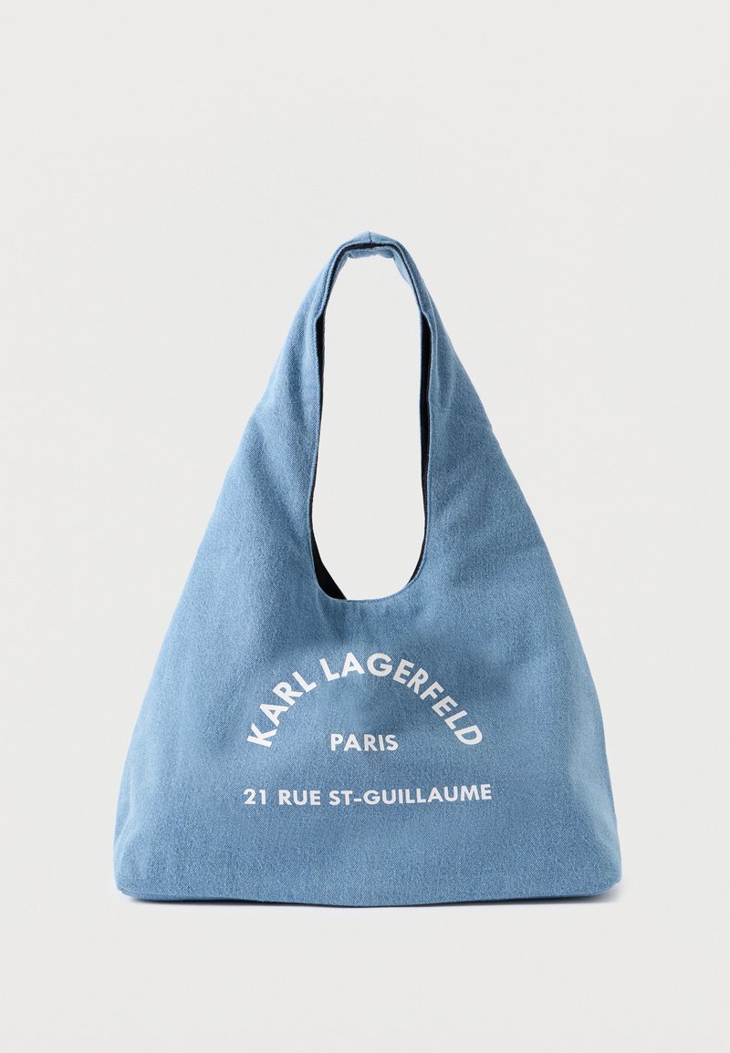 Bolsa de ombro azul em lona com um formato descontraído, apresentando texto branco: "KARL LAGERFELD PARIS 21 RUE ST-GUILLAUME." Textura suave, grande abertura.