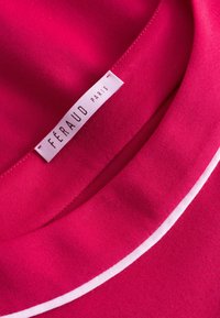 Féraud Paris Etikett auf einem lebhaften pinkfarbenen Stoff mit einer glatten Textur und einem weißen Paspel entlang des Kragens.