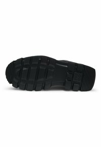 Black rubber shoe sole featuring a textured design with deep treads and a logo embossed on the side for traction and grip.