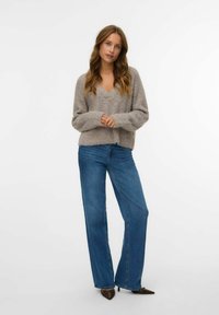 Pull en tricot gris avec un col en V, associé à un jean en denim bleu taille haute. Les jeans ont une jambe droite et large avec des ourlets légèrement effilochés.