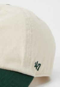 Gorra de algodón beige con visera verde oscura, que presenta un "47" bordado en el lateral, mostrando un patrón de puntada texturizado.
