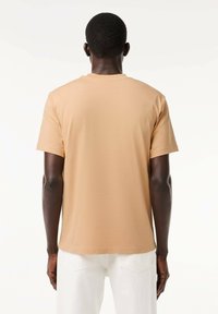 T-shirt corto a maniche corte di un beige chiaro, realizzato in morbido cotone, con colletto rotondo e vestibilità comoda. Texture liscia senza motivi visibili.