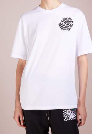 White short-sleeve t-shirt in cotton with a black graphic design on the left chest. Relaxed fit with a crew neck, paired with black pants featuring a patterned pocket.