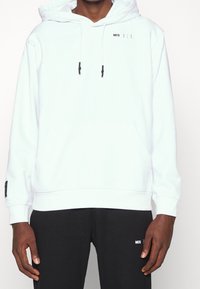 White hoodie with a kangaroo pocket, adjustable drawstrings, and black logo detail on the chest. Soft fabric, relaxed fit, ribbed cuffs.