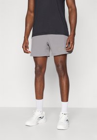 Graue Sportshorts mit einer weichen Textur. Verfügt über ein seitliches Logo in hellem Gold, kombiniert mit weißen Sportschuhen und Kniestrümpfen.