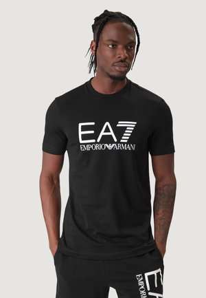 T-shirt nera in cotone con scollo rotondo, logo bianco stampato "EA7 Emporio Armani" sul davanti, maniche corte e design aderente.