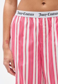 Ριγέ παντελόνια πιτζάμας με λευκή ελαστική μέση που φέρει το λογότυπο "Juicy Couture". Ροζ και κόκκινες κάθετες ρίγες με τρία κουμπιά μπροστά.