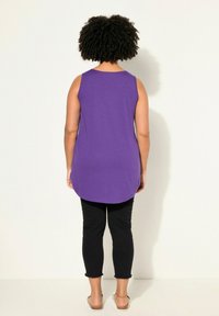 Top viola senza maniche con orlo arrotondato, abbinato a leggings neri alla caviglia con orli sfrangiati. Calzature casual completano l'outfit.