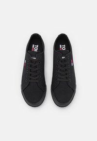 Czarne trampki na płótnie z wiązaniem na sznurówki, gumową podeszwą i fakturowaną powierzchnią. Na języku znajduje się logo w kolorach czerwonym, białym i niebieskim.