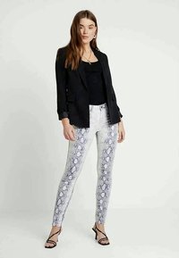 Černé sakové sako přes černý top bez rukávů, doplněné o bílé skinny džíny se vzorem hada a černé stiletto sandály.