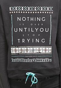 Sudadera negra con un diseño gráfico que incluye texto en blanco y azul verdoso, patrones intrincados y un cordón turquesa en el dobladillo.