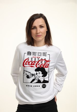 Witte sweatshirt met lange mouwen met een retro Coca-Cola graphic in rood en zwart, waarin een vrouw een glazen fles drinkt.