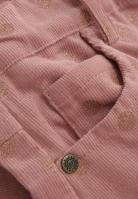 Roze ribfluweel stof heeft gouden glitter stippen en een patchzak, met een metalen knoop die het ontwerp accentueert.
