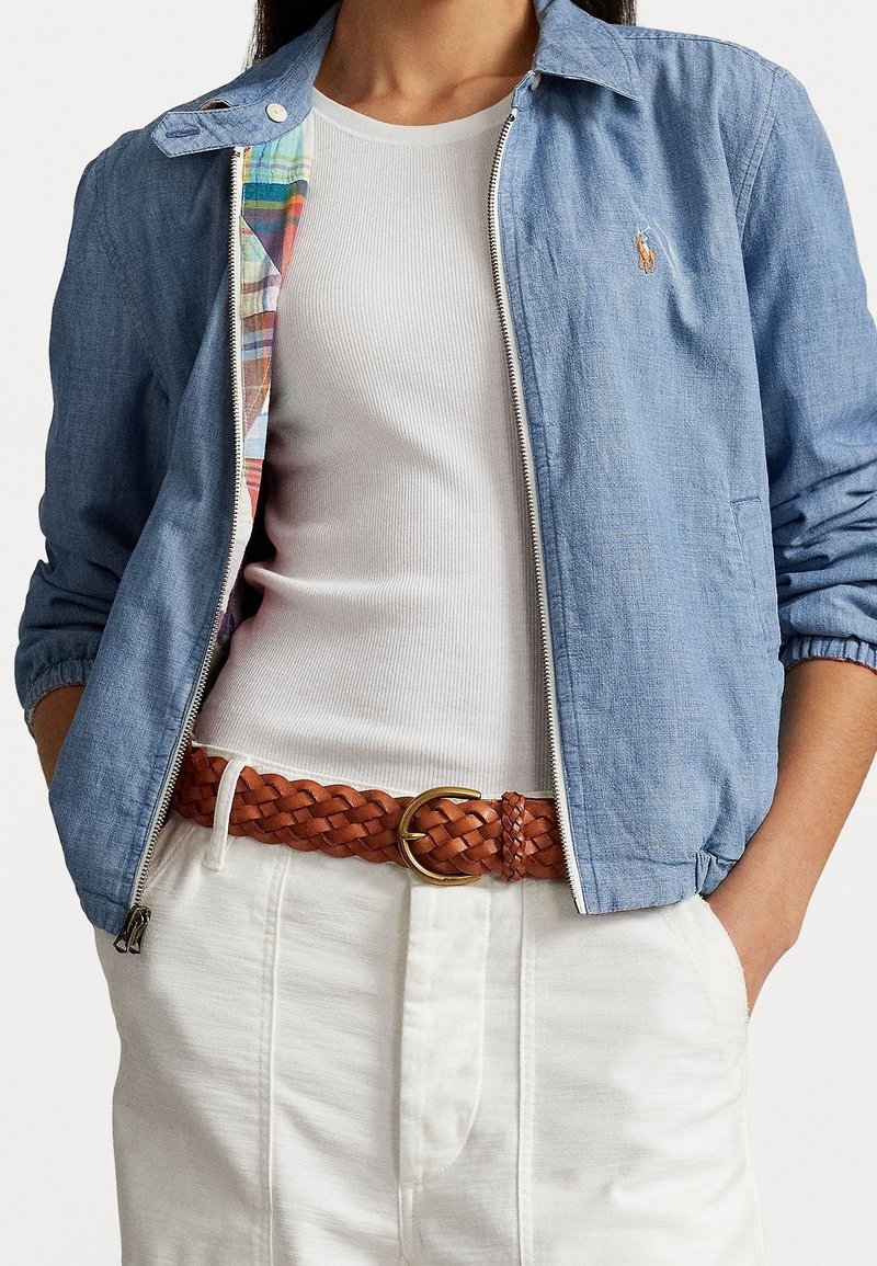Jasnoniebieska kurtka chambray z zamkiem, w kratkę podszewką, ściągaczami na rękawach oraz małym haftowanym logo. Noszona na białym podkoszulku i beżowym plecionym pasku.