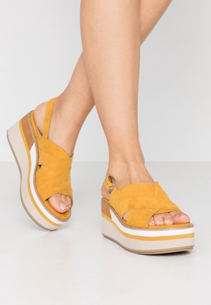 Yellow suede platform sandals with a crossover strap design, featuring a brown and white layered sole and a buckle accent on the heel.