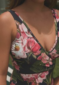 Zwemoutfit met een bloemenpatroon, gekenmerkt door grote roze en witte bloemen op een marineblauwe achtergrond, met een diepe v-halslijn en zwarte stikdetaillering.