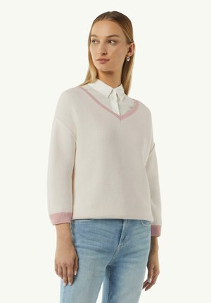 Light pink knitted sweater with a V-neck, featuring a ribbed pink trim on the neckline and cuffs, paired with blue jeans.