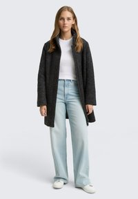 Manteau texturé gris foncé avec un col montant, porté sur un haut blanc, associé à un jean large bleu clair et des baskets blanches.