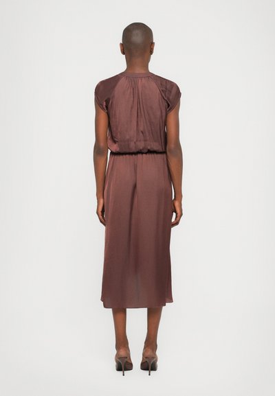Robe en satin marron avec des manches courtes, taille froncée et longueur mi-mollet. Texture lisse et éclat subtil, associée à des talons aiguilles.
