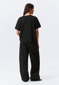 Black, short-sleeve t-shirt with a relaxed fit. Paired with black, wide-leg jeans featuring back pockets and a slightly faded texture.