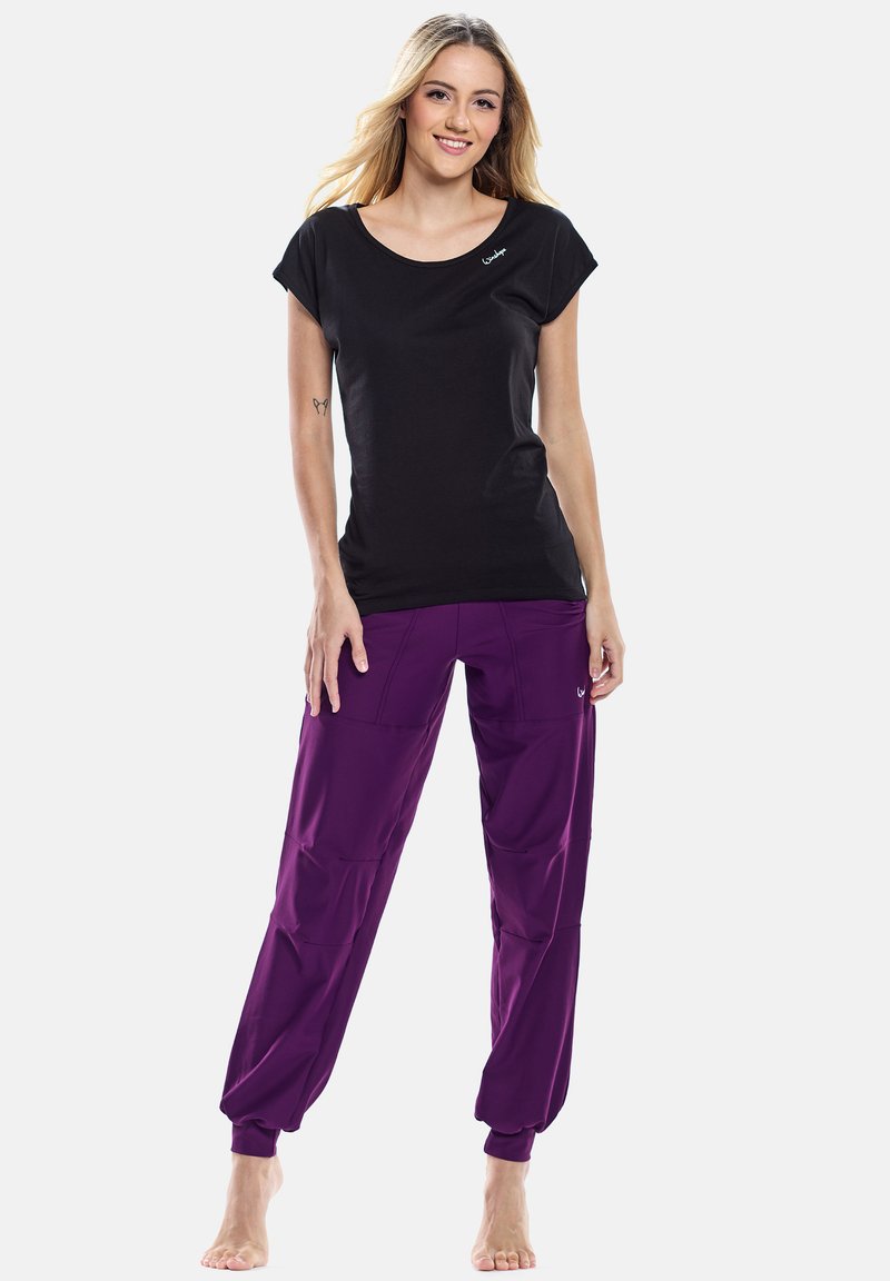 T-shirt nera a maniche corte con scollatura rotonda; abbinata a pantaloni jogger viola con risvolti, dotati di tasche laterali e accento con logo.