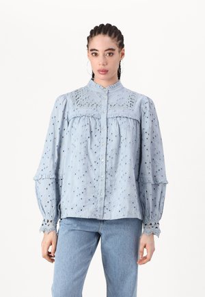 Blusa in cotone azzurro chiaro con motivi a occhiello, colletto e polsini arricciati, e chiusura a bottoni. Maniche lunghe con dettagli in pizzo alle estremità.