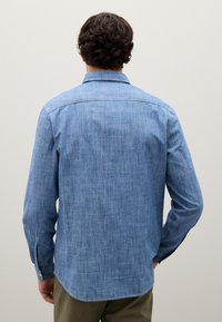 Camisa de botones azul claro, con un patrón texturizado, mangas largas y un cuello. Presenta detalles en los puños con botones y un dobladillo curvado.