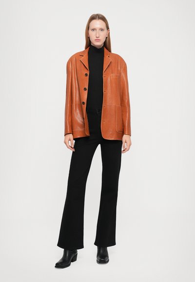 Brown leather blazer with a tailored fit, featuring notched lapels, button closure, and two front pockets. Paired with black turtleneck and pants.