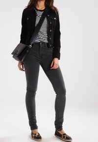 Czarna dżinsowa kurtka na paski, zestawiona z szarymi jeansami skinny i espadrylami w panterkę. Czarna torebka na ramię dopełnia całość.