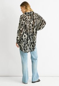 Sheer black and cream shirt with an abstract pattern, long sleeves, and a relaxed fit, paired with light blue flared jeans.