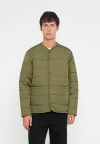 Žalios spalvos siuvinėta striukė su apvaliu apykakle, priekiniais mygtukais, dviem kišenėmis ir subtiliu logotipu kairėje kišenėje. Atsitiktinė fasonas ir tekstūruota medžiaga.