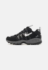 Black sneaker featuring a suede and mesh upper with white accents, zigzag stitching, and a textured rubber outsole for traction.