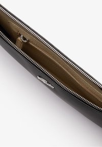 Pochette en cuir noir zippée avec des dents de fermeture éclair en argent, doublure intérieure beige et un compartiment zippé intérieur.