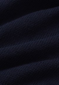 Tissu tricoté bleu marine foncé avec un tissage texturé visible et des plis doux créant des ombres et de la profondeur.