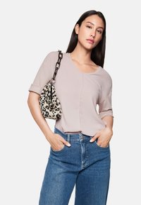 Helles rosa Kurzarmoberteil mit rundem Ausschnitt, kombiniert mit hellblauen Denim-Jeans und einer Handtasche mit Leopardenmuster und Kettenriemen.