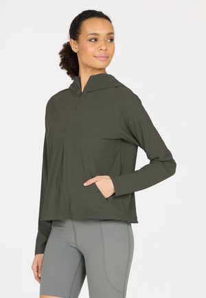 Dunkelgrüner, leichter Pullover-Hoodie mit halbem Reißverschluss auf der Vorderseite, langen Ärmeln und einer Vordertasche. Kombiniert mit hellgrauen, eng anliegenden Shorts.