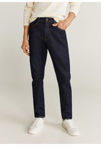 Jeans in denim blu scuro con taglio dritto, caratterizzati da cuciture arancioni a contrasto, chiusura con bottone e tasche frontali. Indossati con sneakers bianche.