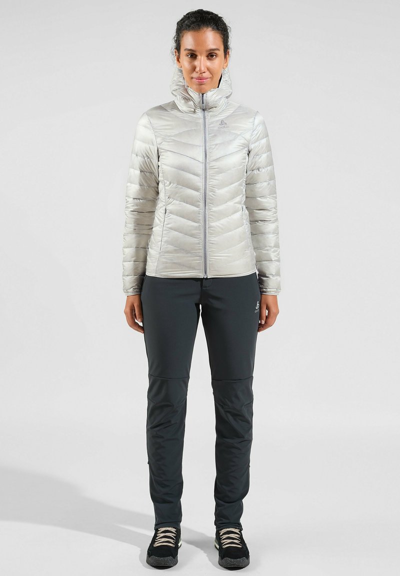 Helle silberne Daunenjacke mit Chevron-Steppung, hohem Kragen und Frontreißverschluss, kombiniert mit dunkelgrauen, schmalen Hosen und schwarzen Wanderschuhen.