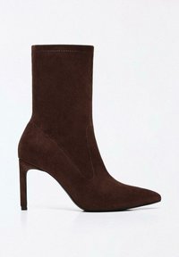 Barna szarvasbőrből készült bokacsizma hegyes orral, magas tűsarokkal, és minimális varrási részletekkel az oldalain. Simafehér textúra.