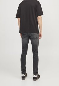 Camiseta de algodón negra combinada con jeans gris oscuro con bolsillos traseros y costuras sutiles. El calzado son zapatillas negras y blancas.