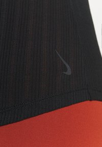 Haut de sport noir avec un design à rayures texturées, arborant un logo Nike noir et une section inférieure rouge, mettant en valeur des couleurs et des matériaux contrastants.
