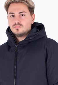 Giacca con cappuccio blu navy con zip frontale, texture liscia e dettagli con cordino. Design semplice e moderno, adatta per un look casual.