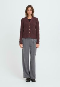 Burgundy cardigan, jossa on teksturoitu neule, V-pääntie, viisi koristepainiketta ja ribbireunukset, yhdistettynä harmaisiin leveisiin housuihin.