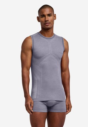 Muskuløs mand iført en tætsiddende grå ærmeløs top og matchende boxerbriefs, der står mod en ensfarvet hvid baggrund.