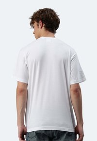 T-shirt bianca in cotone con maniche corte, vestibilità comoda e una piccola etichetta patch sul colletto. Texture liscia, design semplice.