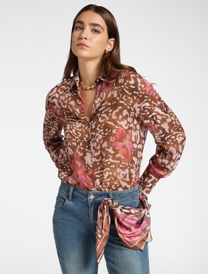 Chemise à motif floral marron en tissu léger, avec des accents roses et violets, associée à un jean bleu et un détail de foulard noué.