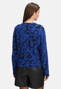 Niebieski i czarny sweter w wzory z okrągłym dekoltem i długimi rękawami, wykonany z teksturowanej tkaniny, w połączeniu z czarnymi skórzanymi szortami.