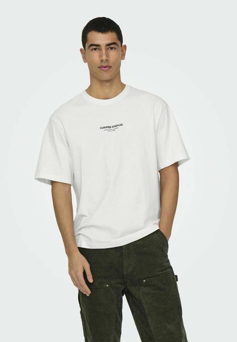 Weißes T-Shirt mit kurzen Ärmeln und schwarzem Text "CURATED STAPLES" auf der Brust. Der Stoff wirkt glatt und leicht.